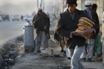 An Afghan man walks with bread as a roadside tea seller is seen in ...