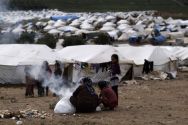 Syrian women who fled their homes start a fire next to their tents at ...