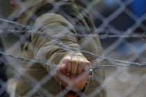 a-migrant-holds-a-barbed-wire-fence-at-the-macedonian-greek-border