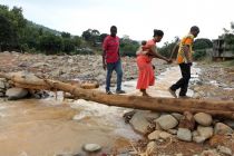 a-man-helps-a-woman-cross-a-log-bridge-after-the-flash-flood-washed-away-a-concrete-bridge-at-pentagon-in-freetown
